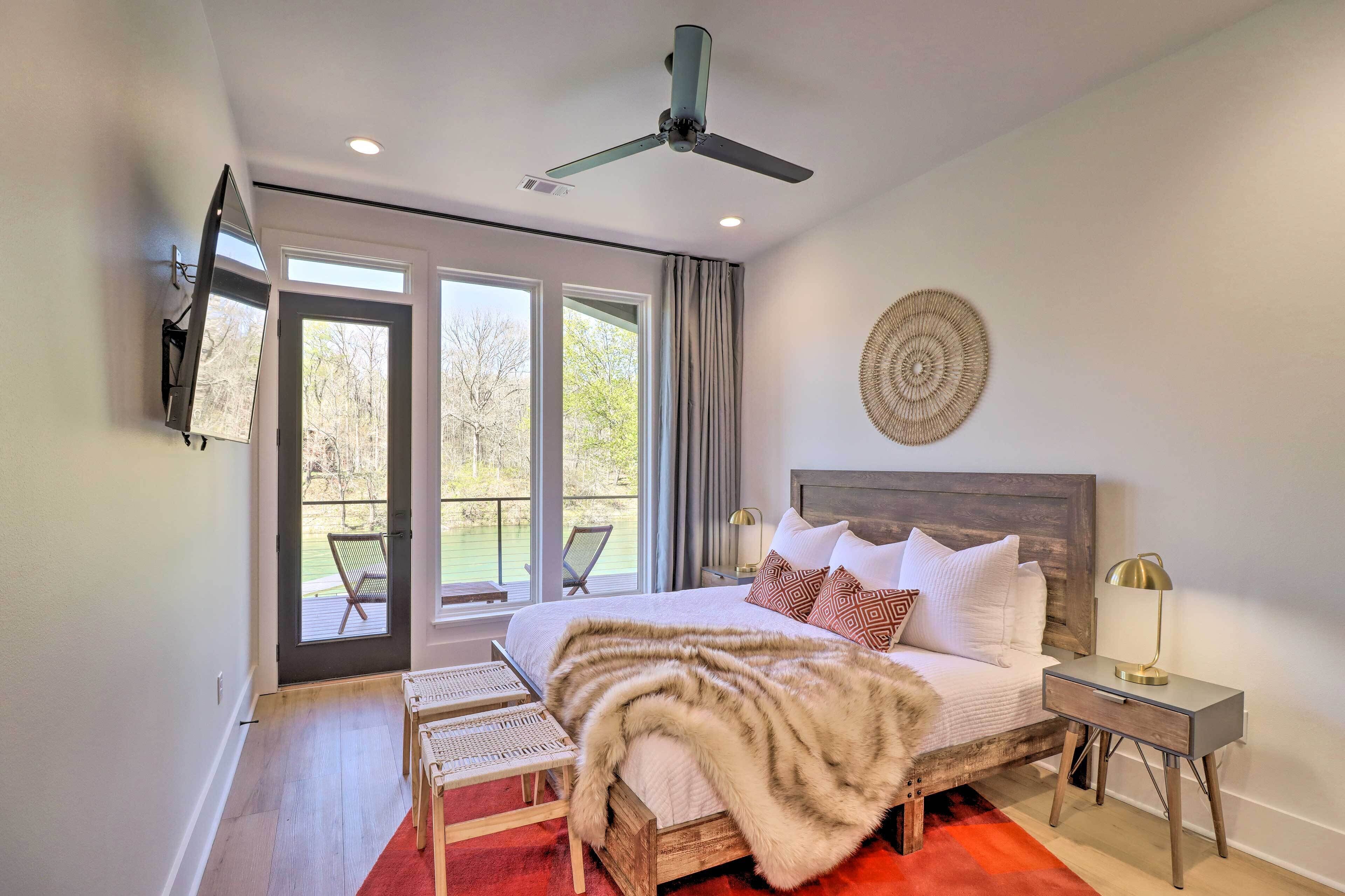A bedroom with a bed, a nightstand, a TV mounted on the wall, a ceiling fan, and a view of the outdoors through a sliding door.