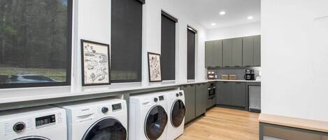 A modern laundry room with four Samsung washing machines, a bench, and framed artwork on the wall.