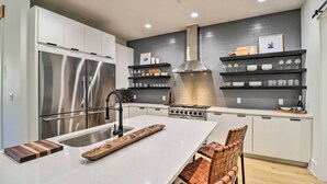 A modern kitchen with stainless steel appliances, a central island, and a brick-patterned chair. - Boat Dock & Slip: Riverfront Home in Heber Springs (Heber Springs)
