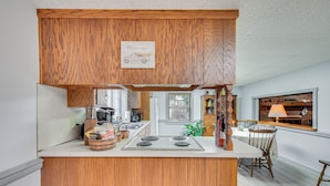A kitchen with wooden cabinetry, a central island with a stove, and a dining area with a table and chairs.
