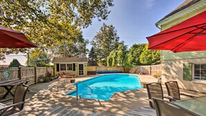 A wooden deck with a swimming pool, outdoor furniture, and a red umbrella.