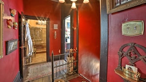 A room with red walls, a chandelier, a mirror, and a door leading to another room. - Vintage Apartment in Historic Downtown La Porte (La Porte)