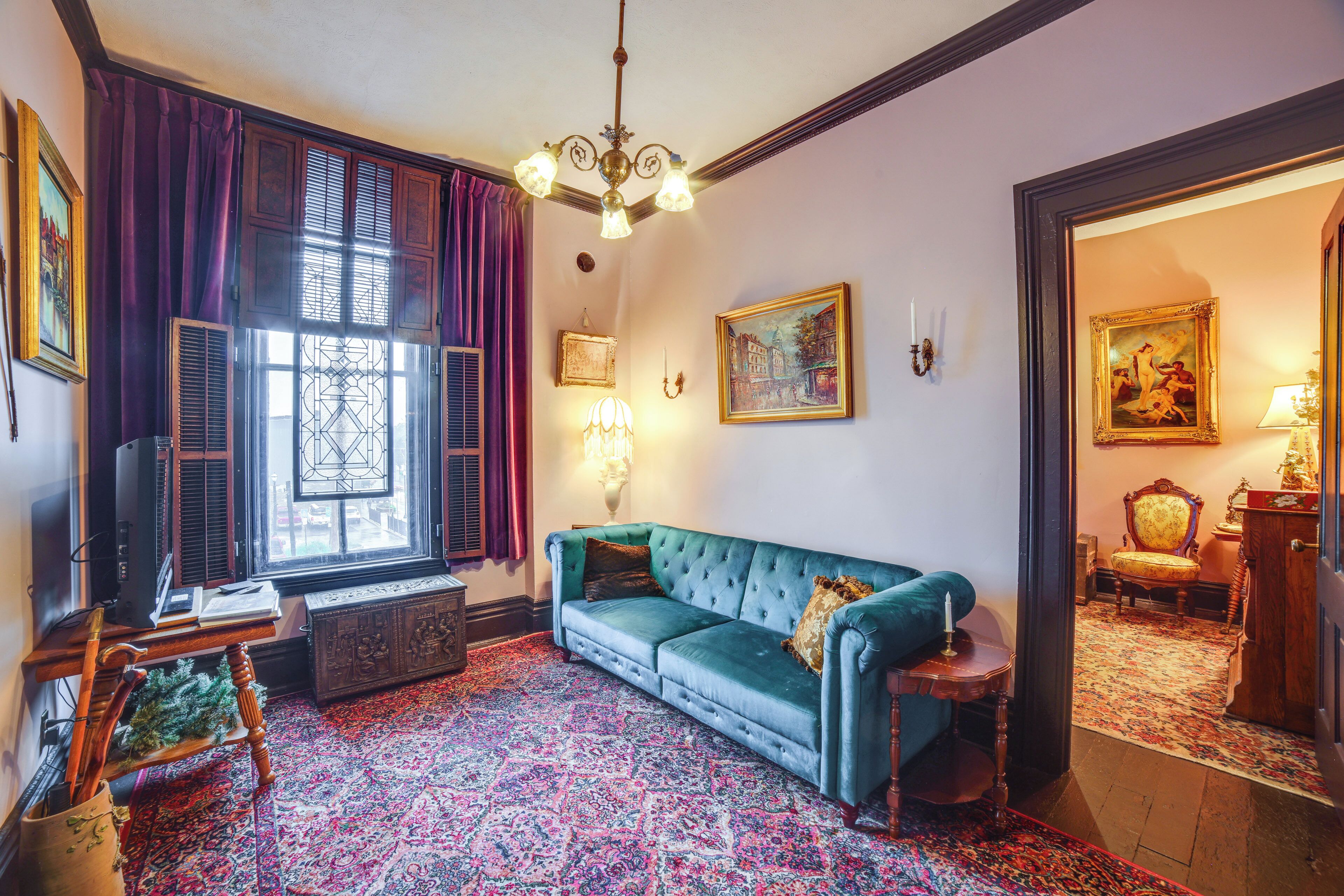 Une pièce avec un canapé de couleur turquoise, une moquette à motifs, un lustre et des œuvres d’art accrochées aux murs.