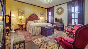 A bedroom with a large bed, a red armchair, a wooden chest, and a chandelier. - Vintage Apartment in Historic Downtown La Porte (La Porte)