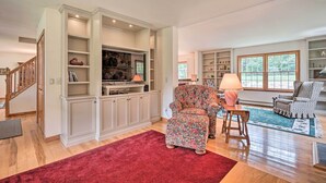 A spacious living room with a large entertainment unit, two patterned armchairs, a wooden coffee table, and a red rug. - Wilmington Home on 18 Acres ~ 9 Mi to Skiing! (Wilmington)
