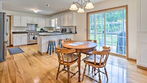 A spacious kitchen with white cabinets, a wooden dining table with chairs, and a large window offering a view of greenery. - Wilmington Home on 18 Acres ~ 9 Mi to Skiing! (Wilmington)
