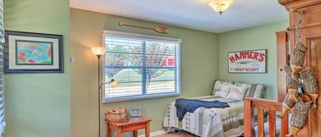 Un dormitorio con una cama, una ventana con persianas, una lámpara, un cuadro enmarcado y un cartel en la pared.