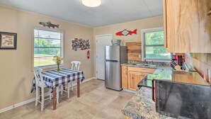 Una cocina compacta con refrigerador, armarios de madera, encimera de granito y un comedor con mantel a cuadros.