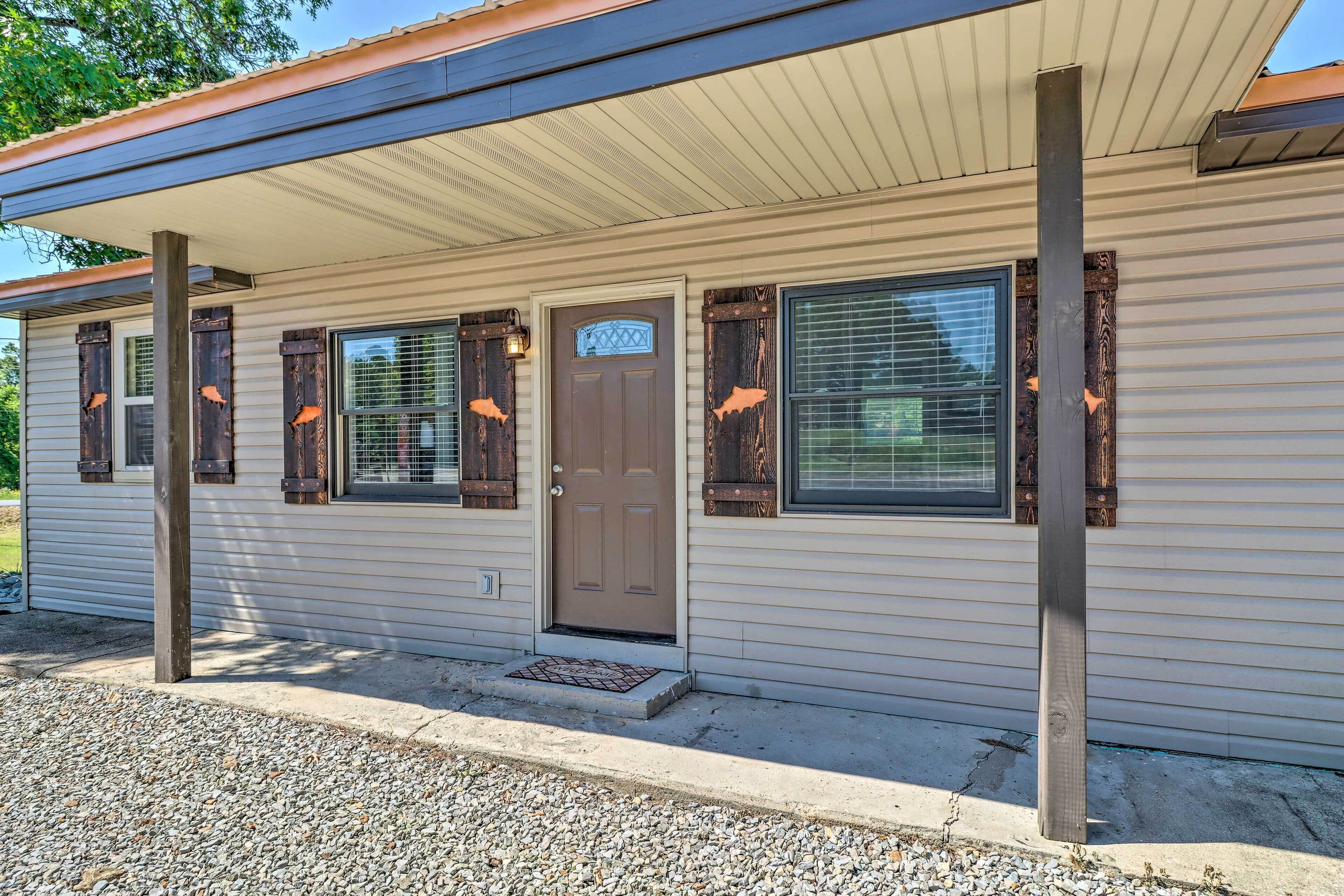 A single-story mobile home with a covered porch, a front door, and two windows with shutters.