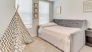 Un dormitorio con cama, una ventana con persianas, un estante con adornos y un cuadro en la pared.