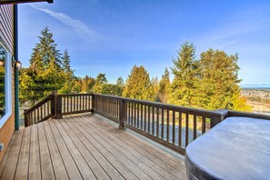 Une terrasse en bois dotée d’une rambarde, offrant une vue sur une zone boisée et, au loin, sur le paysage urbain.