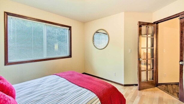 A bedroom with a bed, a window with blinds, a door, and a wall-mounted circular mirror. - Stunning Sequim Hideaway w/ Hot Tub & Views (Sequim)