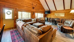 Un interior de cabaña acogedor con un techo de madera grande, un sofá modular, un comedor y un televisor.