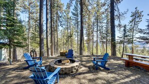 Un área boscosa con un brasero, sillas Adirondack azules y mesas de picnic.