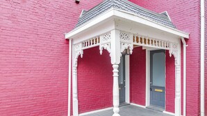Ein rotes Backsteingebäude mit einer weißen Veranda und einer blauen Tür.