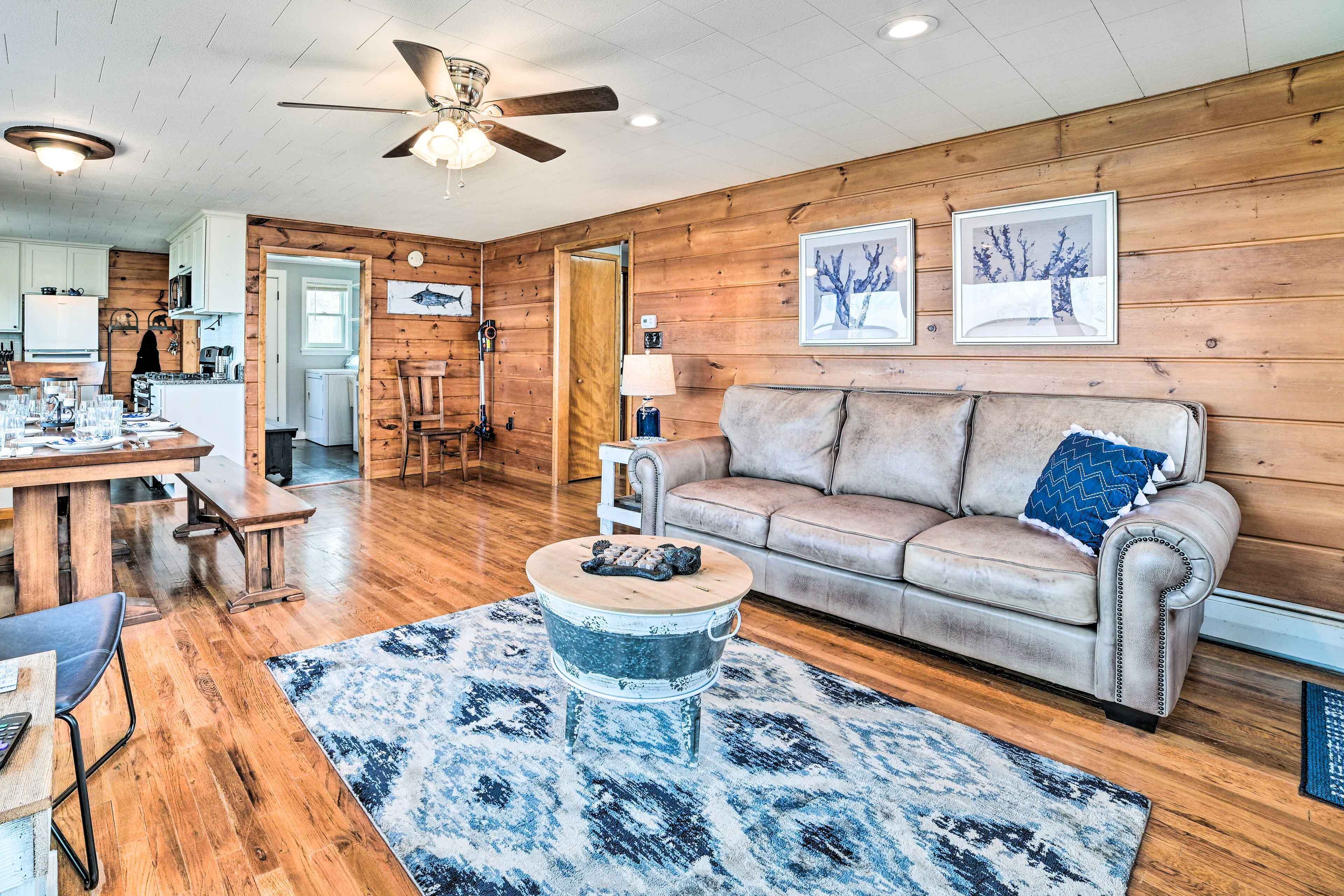A cozy living room with a wooden floor, a leather sofa, a coffee table, and a dining area with a table and chairs.