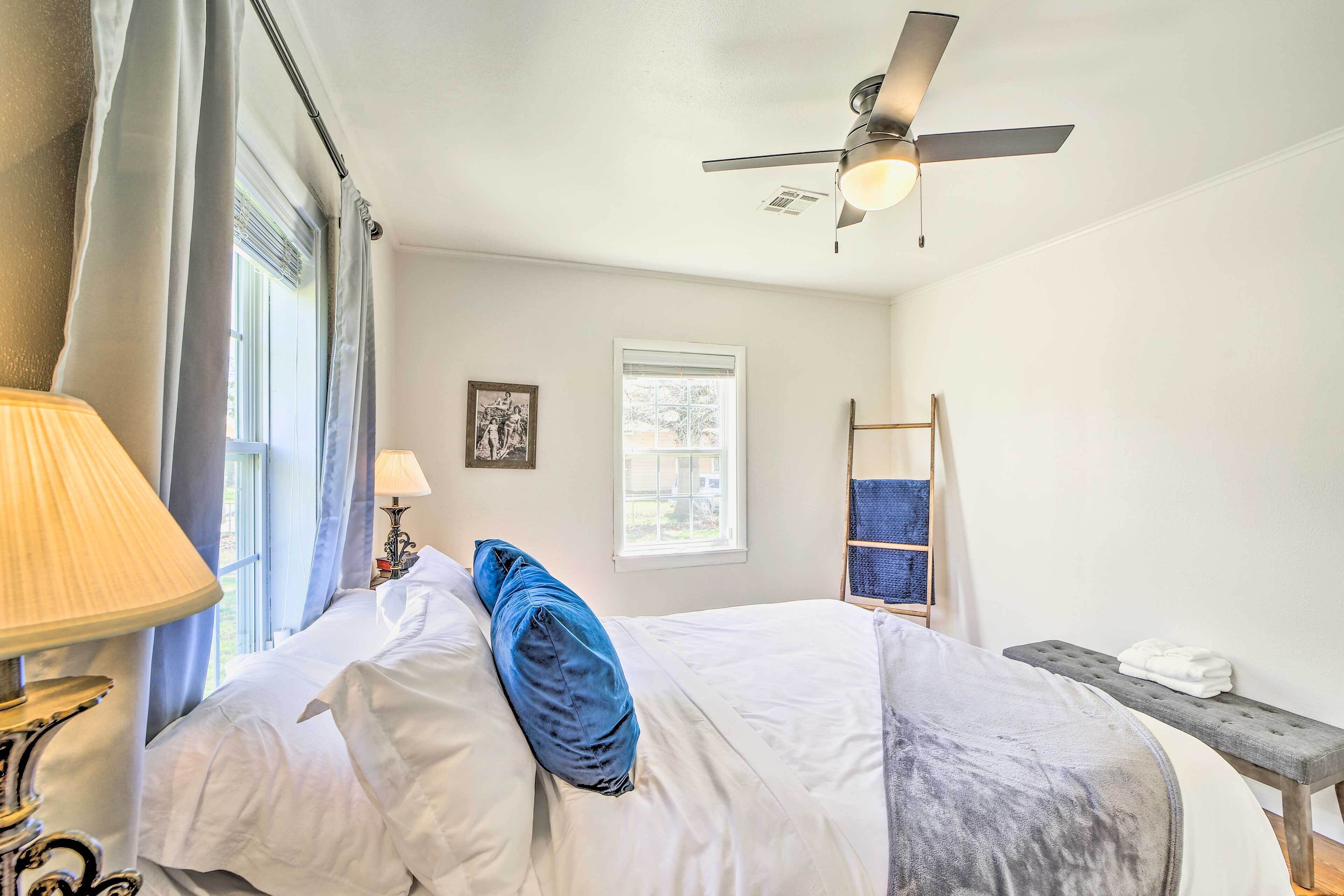 A bedroom with a bed, a ceiling fan, a window, a bedside table with a lamp, and a bench with towels.