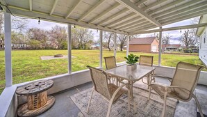 Une terrasse couverte avec une table et des chaises, une bobine décorative et une vue sur une pelouse et des maisons.