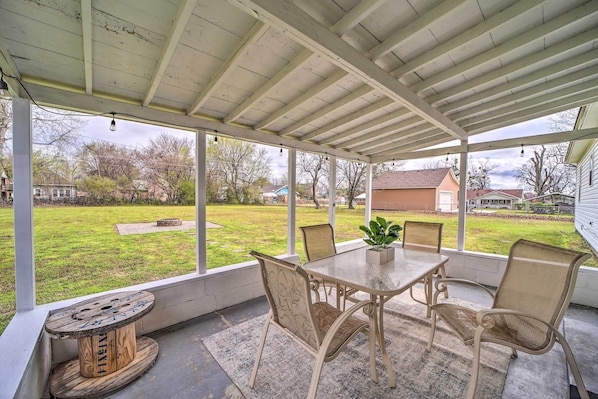 A covered patio with a table and chairs, a decorative spool, and a view of a grassy yard and houses.