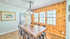 Un espace repas avec une table et des chaises en bois, de grandes fenêtres et un ventilateur de plafond.