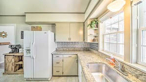 Une cuisine avec un réfrigérateur blanc, un four encastré, un plan de travail en granit, un évier en acier inoxydable et une fenêtre donnant sur l’extérieur.