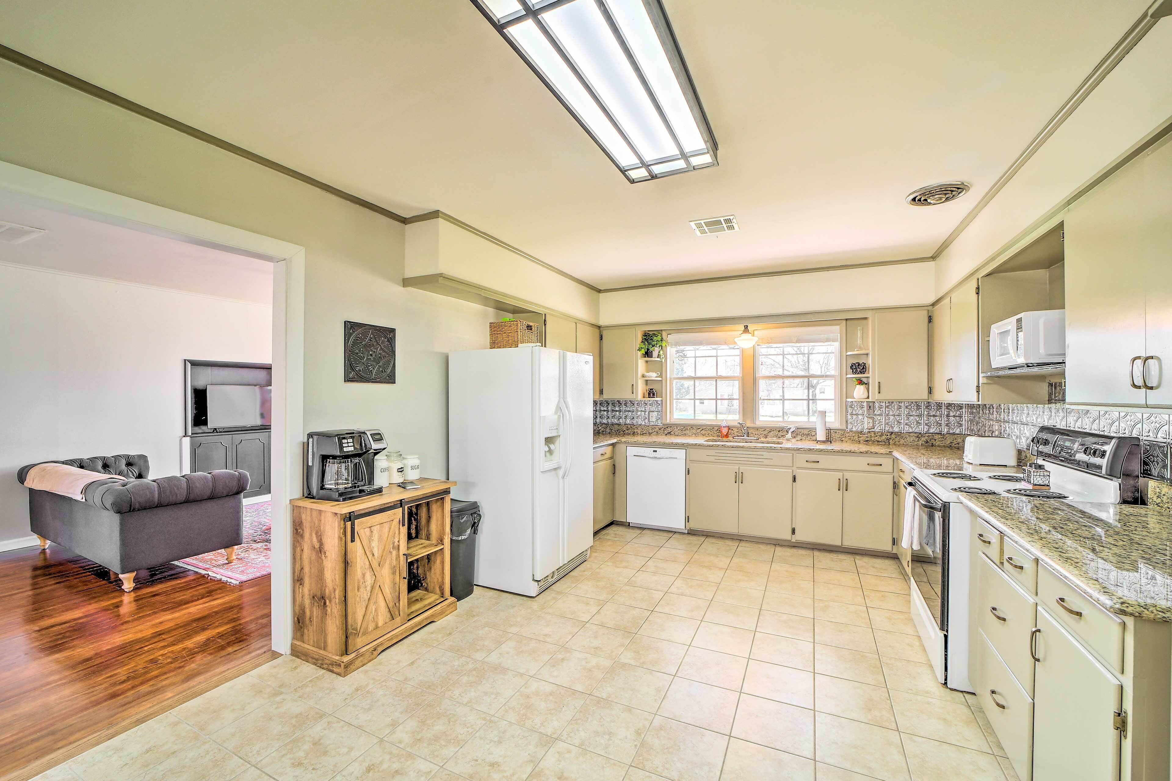Una cocina amplia con refrigerador, microondas y estufa. Hay un comedor con un sofá y una mesa de centro. La cocina tiene un ventanal y una lámpara en el techo.