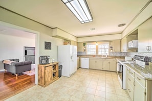 A spacious kitchen with a refrigerator, microwave, and stove. There is a dining area with a couch and a coffee table. The kitchen has a large window and a ceiling light.