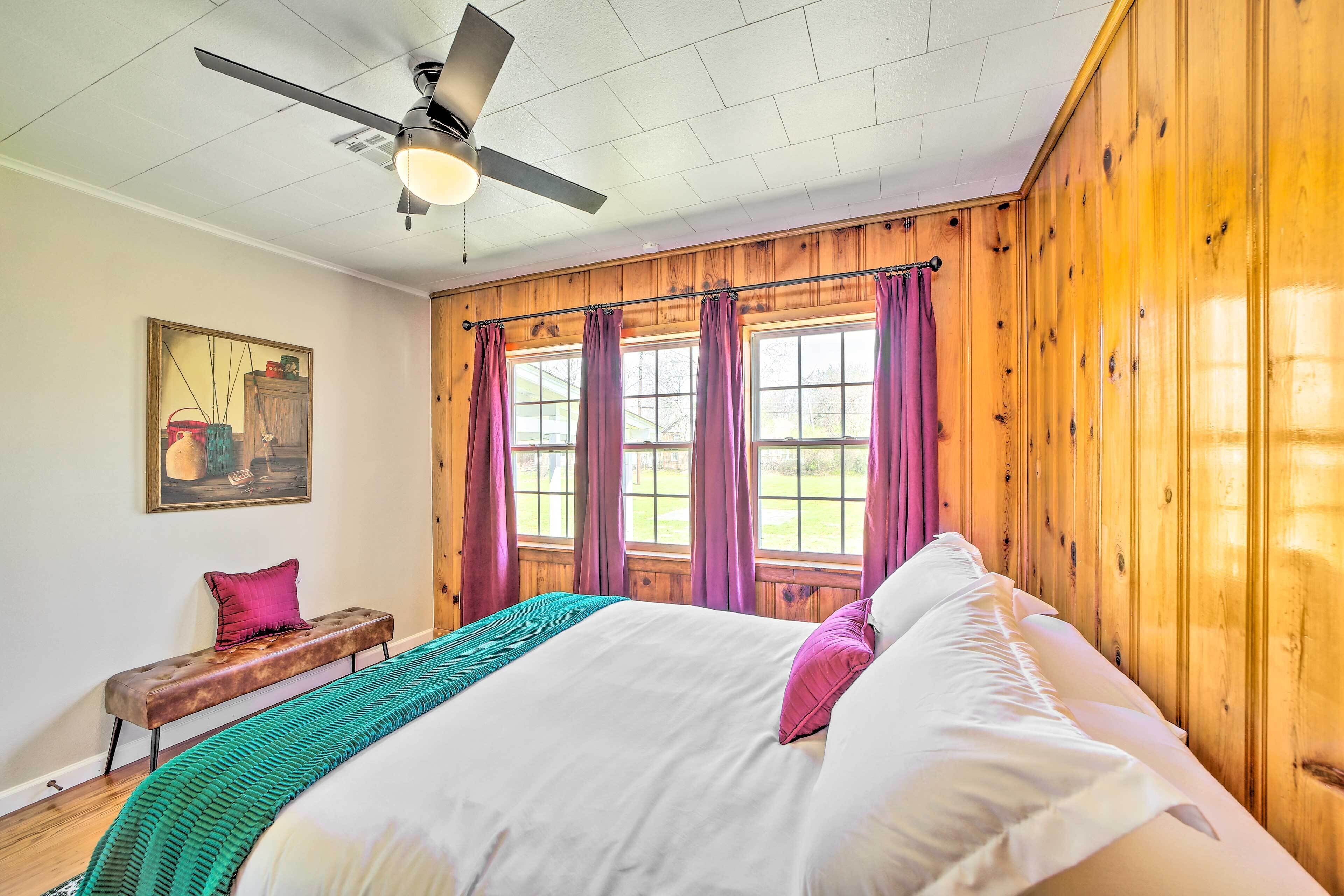 Un dormitorio con una cama grande, un ventilador de techo, paredes de madera y una ventana con cortinas.