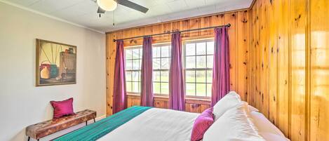 Un dormitorio con una cama grande, un ventilador de techo, paredes de madera y una ventana con cortinas.