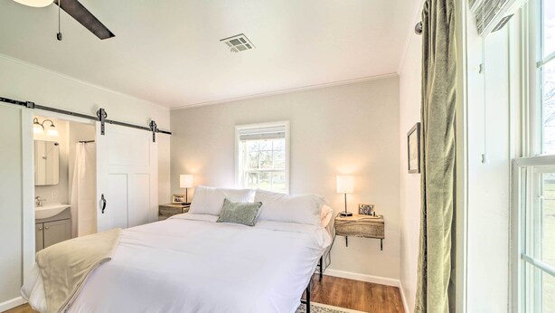 Une chambre à coucher avec un grand lit, des tables de chevet avec des lampes, une fenêtre avec des rideaux et un ventilateur de plafond.