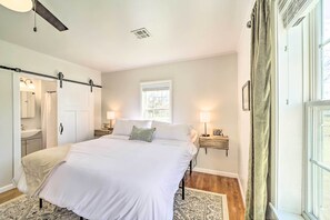 Une chambre à coucher avec un grand lit, des tables de chevet avec des lampes, une fenêtre avec des rideaux et un ventilateur de plafond.