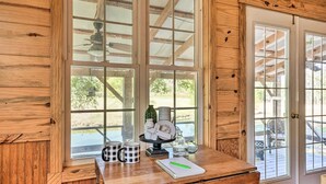 Un intérieur en bois avec un bureau, un ventilateur de plafond et une vue à travers une porte vitrée.