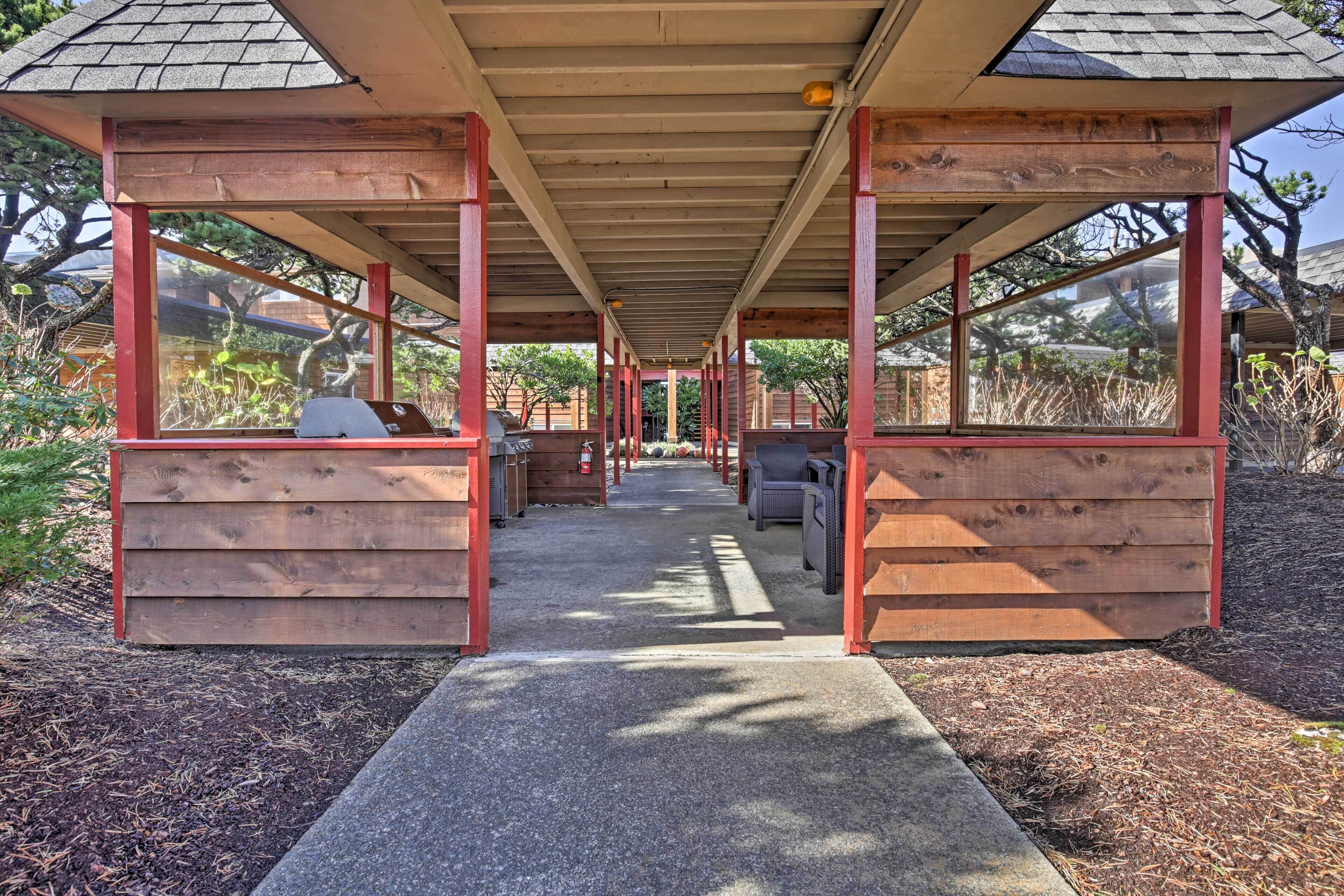 A covered outdoor seating area with wooden benches and tables, surrounded by wooden walls and large windows.