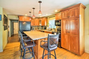 A kitchen with wooden cabinets, a central island with bar stools, a refrigerator, and a microwave. - Walk to Beach: Maine Home w/ Hot Tub & Deck! (Old Orchard Beach)