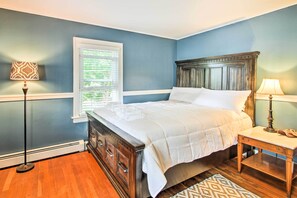 A bedroom with a wooden bed, a nightstand, a floor lamp, and a window with blinds. - Walk to Beach: Maine Home w/ Hot Tub & Deck! (Old Orchard Beach)