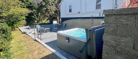 Un jacuzzi en un patio trasero con terraza de madera y mobiliario exterior.