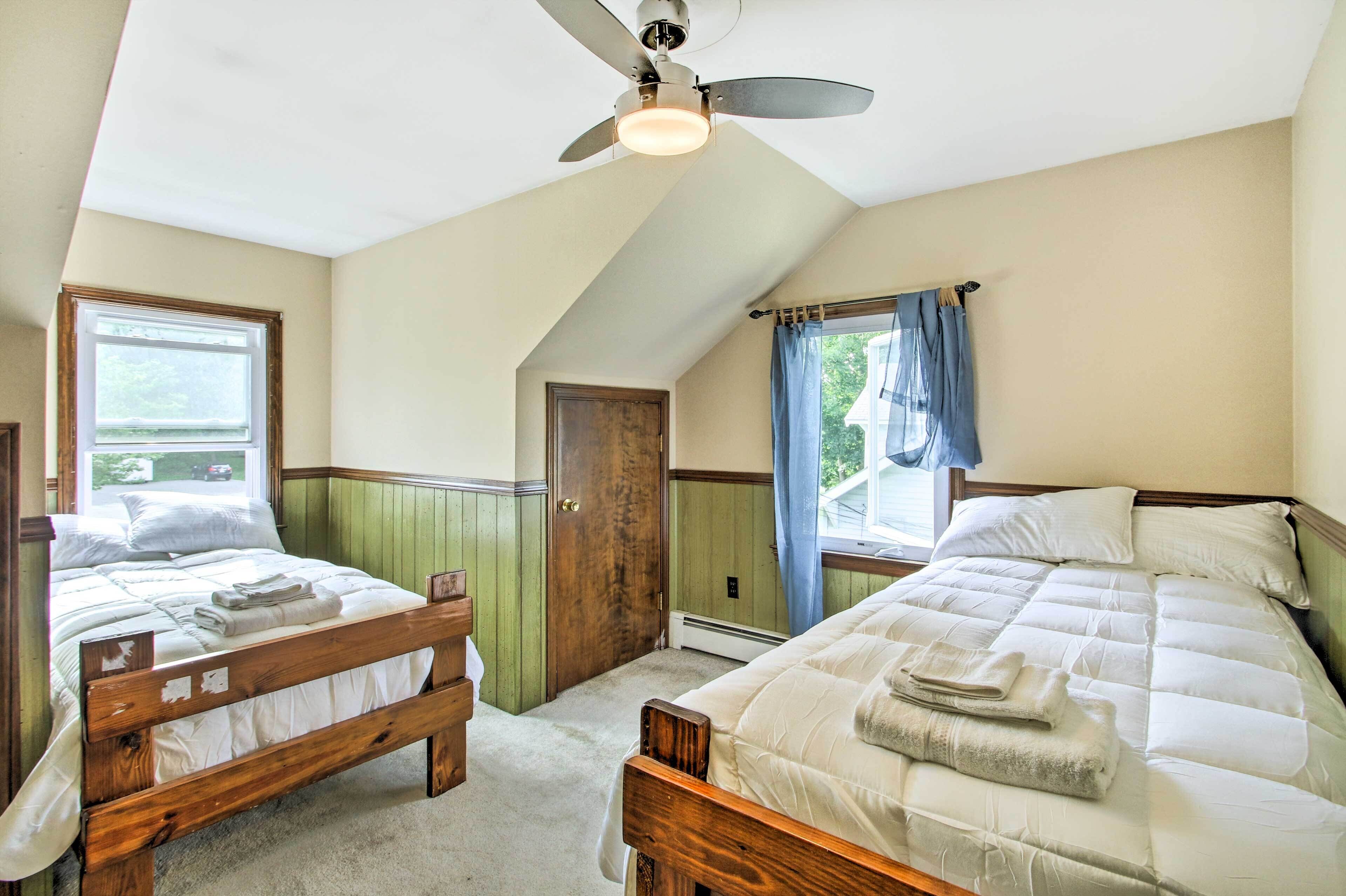 A bedroom with two wooden beds, a ceiling fan, and a window with curtains.