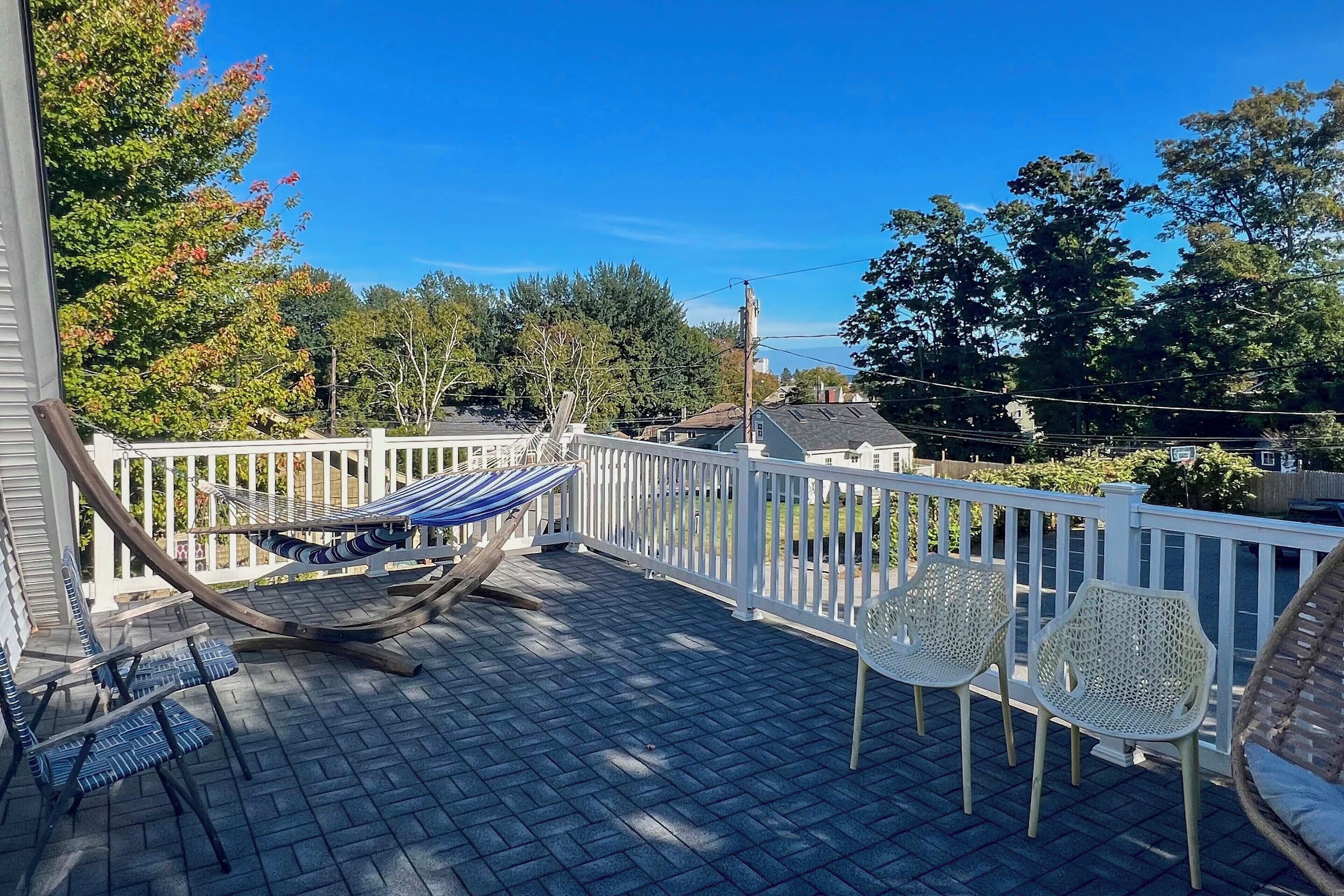 A covered patio with a hammock, chairs, and a white railing.
