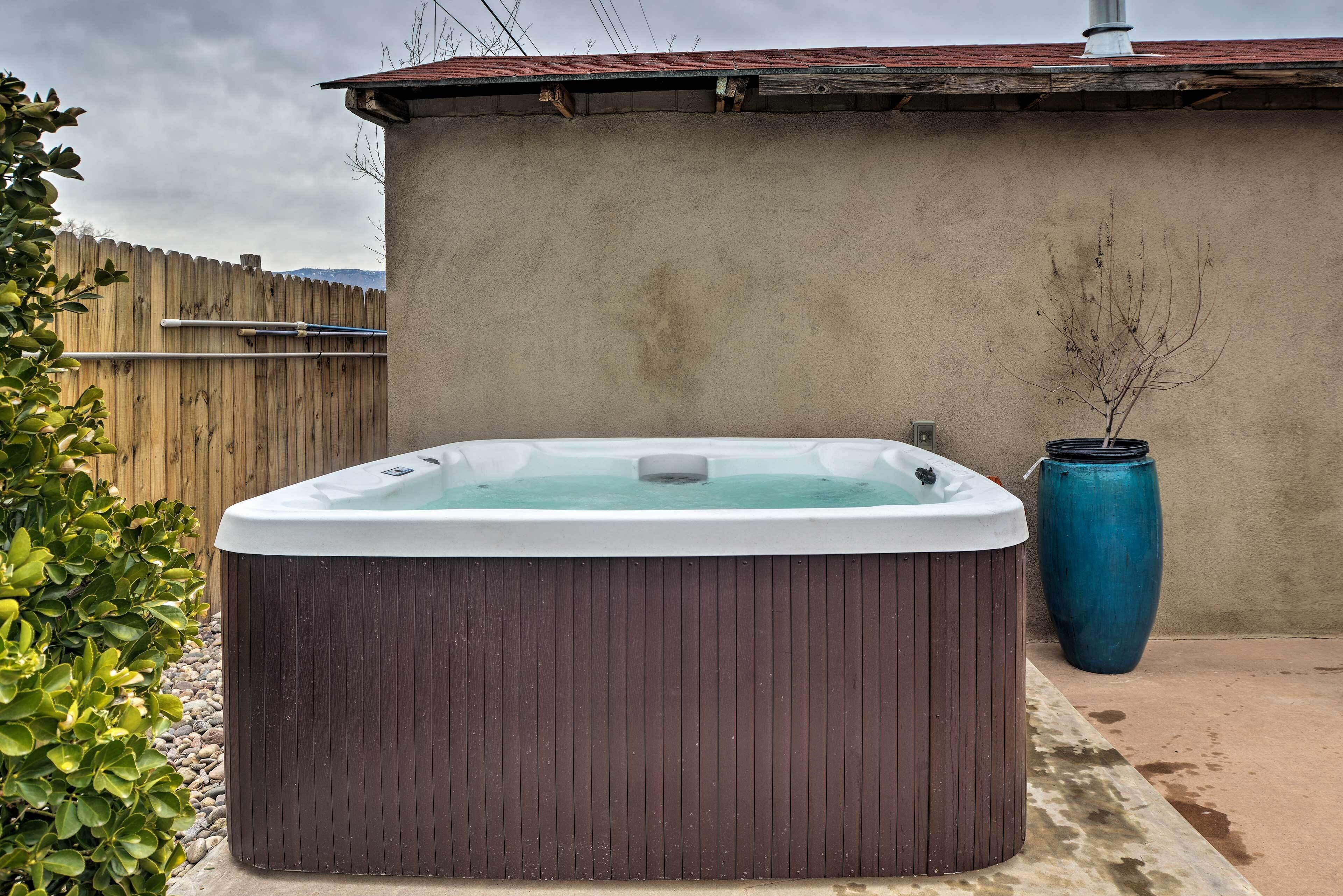 A hot tub in an outdoor setting with a wooden fence, a concrete wall, and a blue vase.