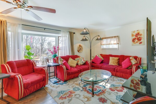 A living room with two red sofas, a glass coffee table, and a ceiling fan.