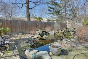 A backyard with a small pond, rocks, a wooden fence, and a bench.