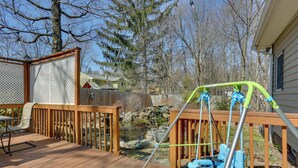 Une terrasse en bois avec une balançoire, un petit étang et une chaise.