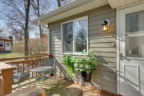 A wooden deck with a chair and a table, a potted plant, and a house with a window and a door.