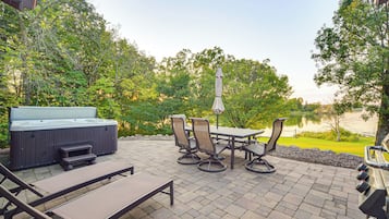 An outdoor patio with a hot tub, lounge chairs, and a table with chairs.