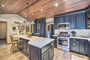 Une cuisine avec des meubles de couleur sombre, un grand îlot central, des appareils électroménagers en acier inoxydable et un revêtement de sol en bois.