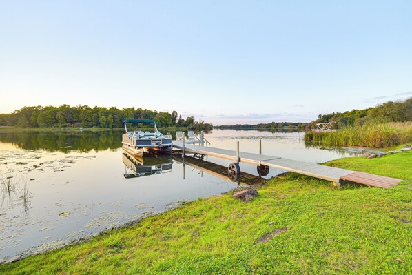 A boat docked at a pier with a grassy area and trees in the background. - Patio, Views & Hot Tub: Quiet Lakeside Cabin (Grantsburg)