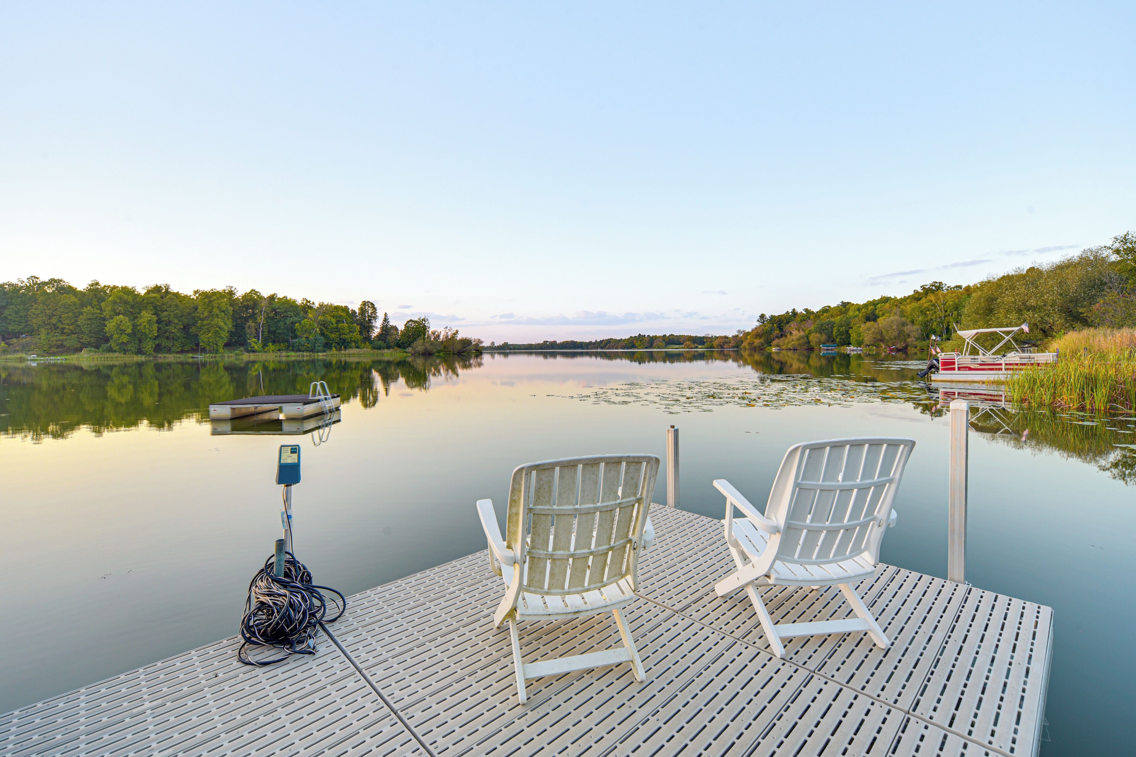 A wooden dock with two white chairs and a fishing rod.