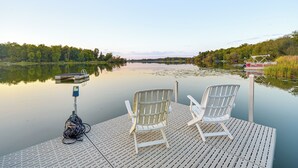 Une jetée en bois avec deux chaises blanches et une canne à pêche.