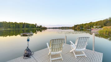 A wooden dock with two white chairs and a fishing rod.