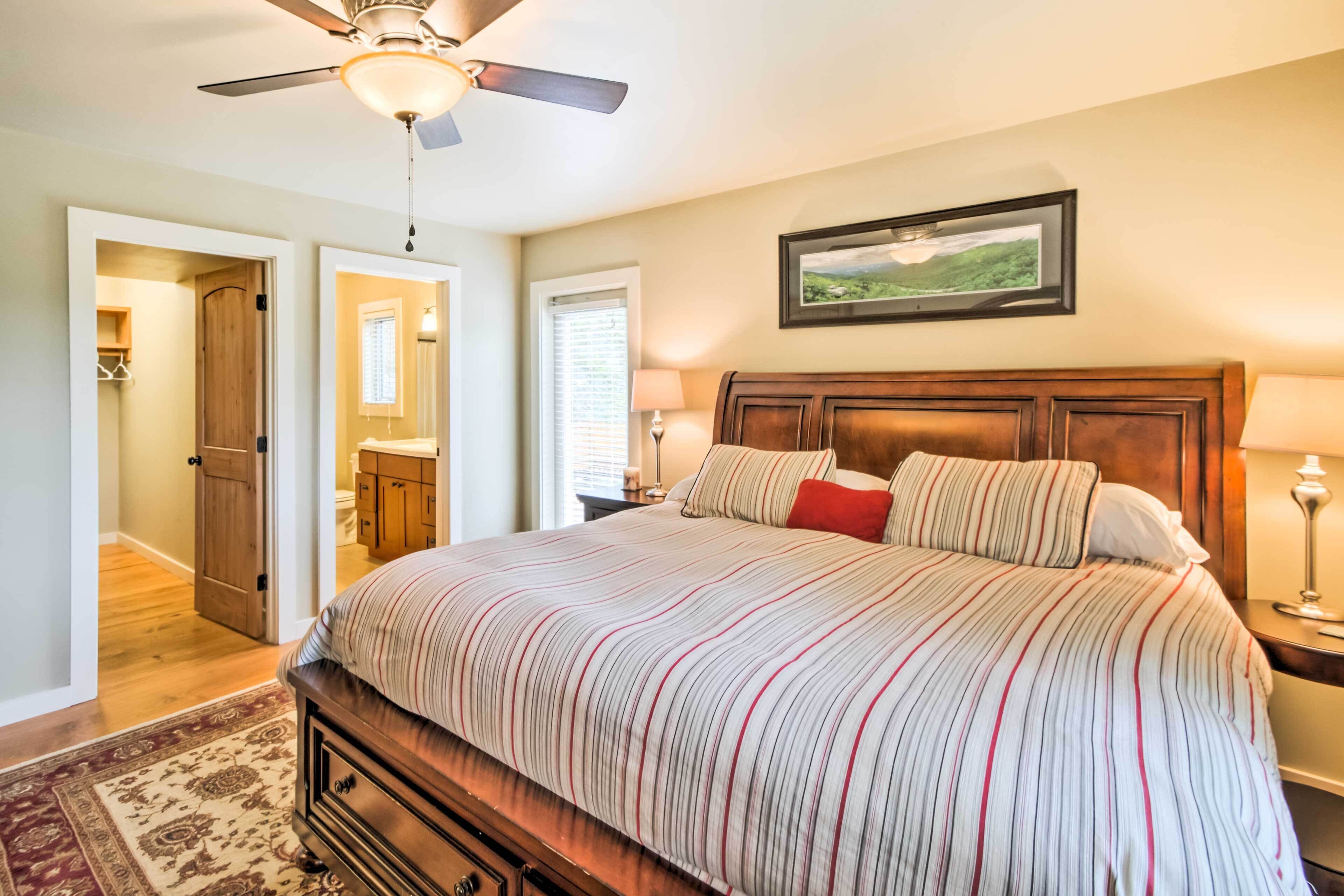 A bedroom with a large bed, wooden headboard, a ceiling fan, and a framed landscape picture on the wall.